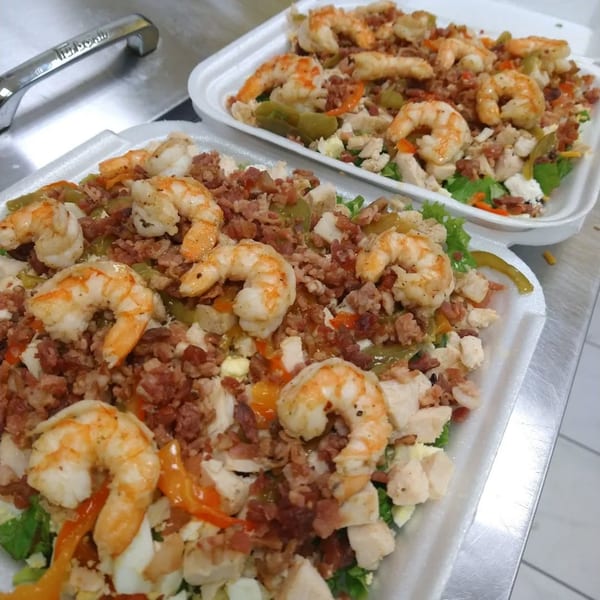 Two healthy shrimp salads with bacon, chicken, and vegetables in white to-go containers.