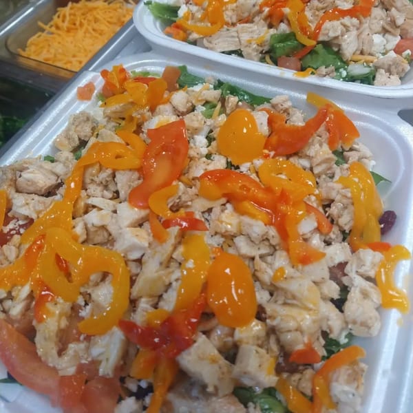 Two healthy salads with chicken, bell peppers, and cheese in white takeout containers.