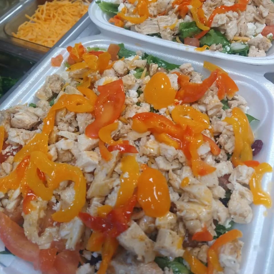 Two healthy salads with chicken, bell peppers, and cheese in white takeout containers.